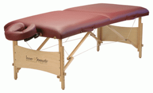 Portable massage table with a padded maroon surface, wooden frame, and an adjustable face cradle attachment.