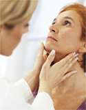 A female doctor in a white coat gently palpates the neck of a patient during a physical examination.