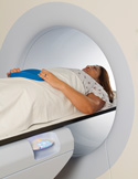 A woman lies on a medical table entering a circular white MRI or CT scanner.