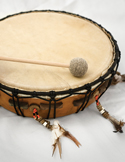 A wooden frame drum with a natural hide surface and a felt-tipped mallet resting on top.