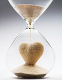 An hourglass with sand forming the shape of a heart in the bottom bulb.