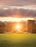 Sunlight glowing through the ancient stone pillars of Stonehenge under a cloudy sunset sky.