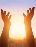 Two hands reached upward toward a bright, glowing sun in a soft purple and orange sky.