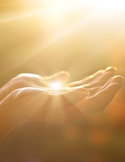 Close-up of two open hands cupped together, filled with a bright, ethereal golden light and sunbeams.