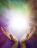 Two hands reaching upward toward a bright, glowing white light surrounded by a colorful, ethereal aura.