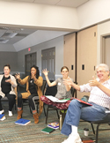A diverse group of people sitting in a circle during a workshop, gesturing with their hands as they learn.