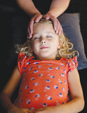 A young girl with closed eyes receives a gentle Reiki healing session with hands placed near her head.