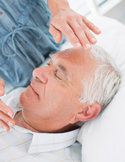 Close-up of a practitioner's hand hovering over the forehead of an elderly man during a healing session.