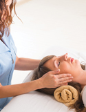 A practitioner gently places her hands on a woman's face during a myofascial release therapy session.