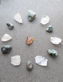 Various raw crystals and gemstones arranged in a circular healing grid on a grey textured surface.