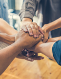 A close-up of a diverse group of people placing their hands together in a stack to show unity and support.