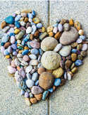 Various smooth, multi-colored river stones arranged on the ground in the shape of a large heart.