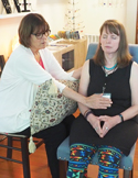 A Reiki practitioner places her hand on the chest of a seated woman who has her eyes closed.