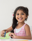 A young girl with a long braid smiles brightly while cutting green paper during an activity.