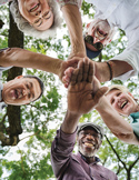 Low-angle shot of a diverse group of smiling seniors standing in a circle with their hands joined.