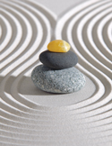 Three smooth stones stacked in a cairn on top of white sand with raked concentric circles.