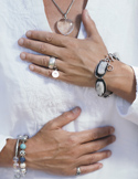 Close-up of a person in white clothing with hands placed over their heart and solar plexus in a healing pose.