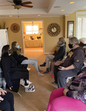 A small group of people wearing face masks sit in a circle during a Reiki class in a living room.