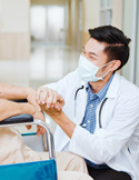 A doctor wearing a face mask holds the hand of a patient in a wheelchair to offer comfort.