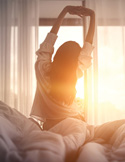 Silhouette of a woman stretching in front of a bright window as the morning sun shines through.