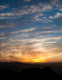 A peaceful landscape at sunset featuring a glowing orange horizon and wispy clouds in a blue sky.