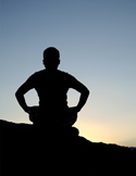 Silhouette of a person sitting in a meditative pose on a rock against a clear, twilight sky.