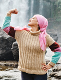 A woman in a pink headscarf flexes her arm in a strong pose in front of a misty waterfall.