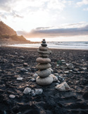 A stack of balanced stones on a black sand beach during a calm sunset.