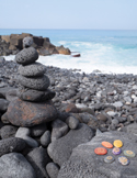 A stack of smooth stones on a rocky beach with ocean waves behind, symbolizing balance, calm, and healing.