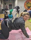 Smiling woman in a playful yoga or stretch pose indoors, surrounded by colorful art and personal items.