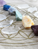 Assorted crystals and gemstones arranged on a cloth printed with a sacred geometry Flower of Life pattern.