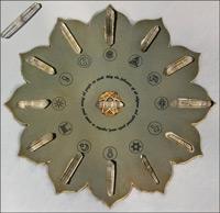 Circular, flower-shaped metallic display with embedded crystal-like pieces and various spiritual or symbolic icons arranged around the center.