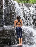 A woman in athletic wear stands before a cascading waterfall, looking up at the falling water.