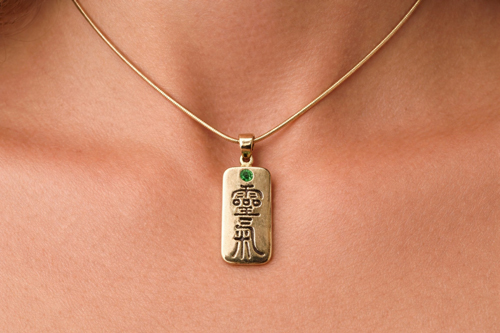 Gold necklace with a rectangular pendant featuring black Reiki Kanji being worn.