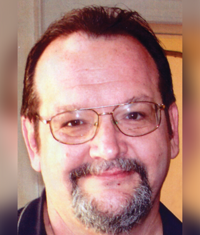 Smiling man with glasses, short dark hair, and a goatee, facing the camera indoors.