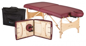 Portable massage table in burgundy with wooden legs, shown folded open with accessories stored inside and a carrying case beside it.