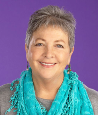 Smiling woman with short gray hair, turquoise scarf, and purple background.